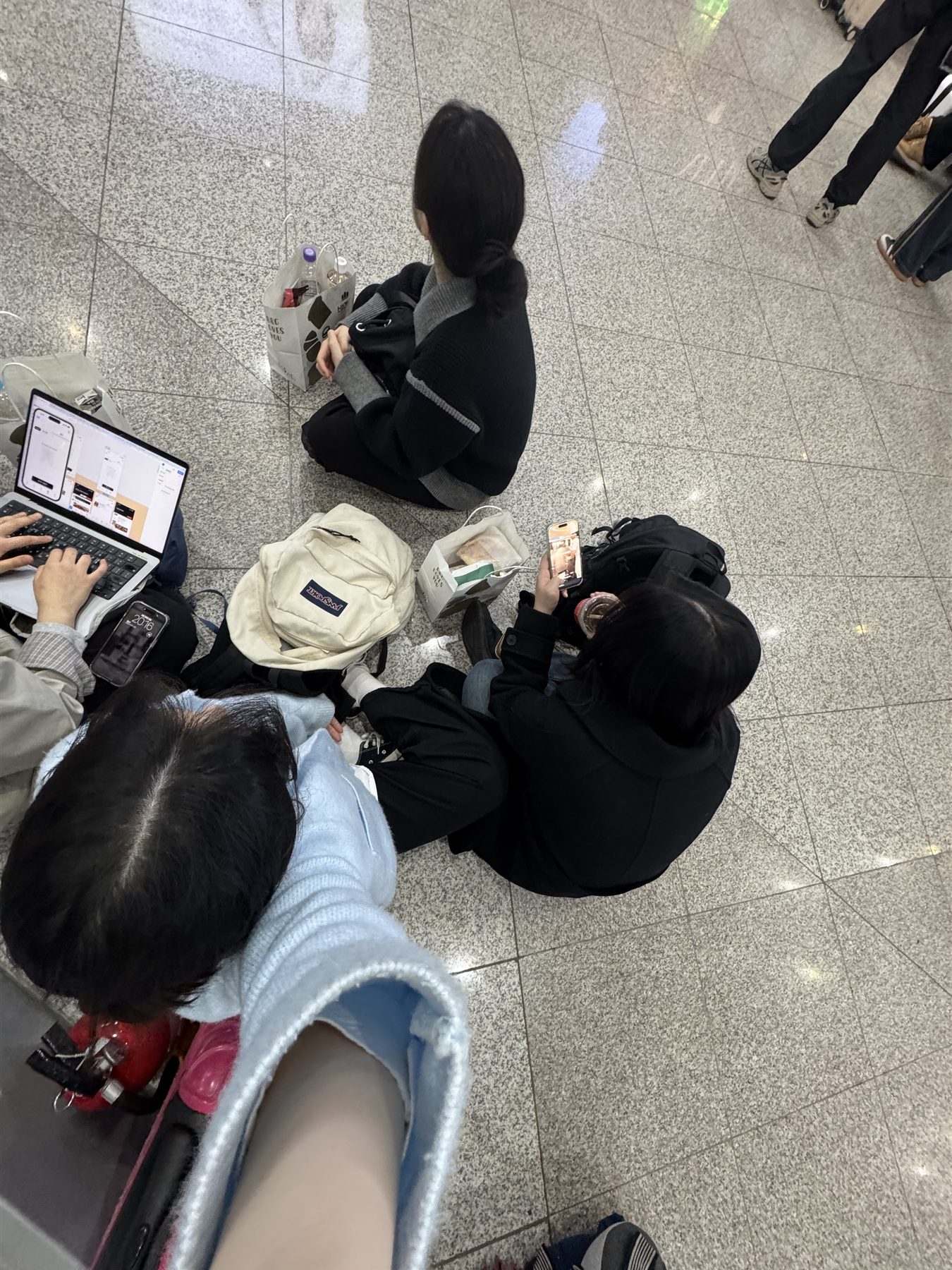 역 대합실 바닥에 앉아 노트북과 휴대폰을 보고 있는 팀원들